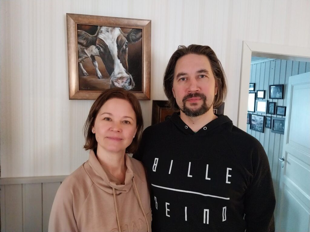 Outi ja Tero Lahti lehmätaulun edessä olohuoneessa. 