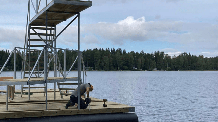 Hyppytornin rakentamista vähäjärvellä. Mies poraa tornia laituriin.