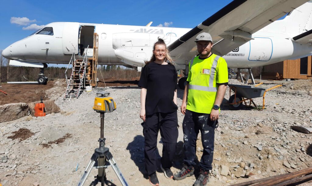 Nuori nainen ja mies seisovat vanhan pienlentokoneen vieressä.