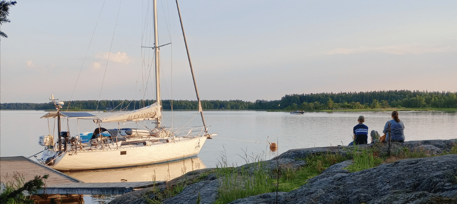 Merimaisema iltahämärässä. Ihmiset istuvat kalliolla ja vene on rannassa.