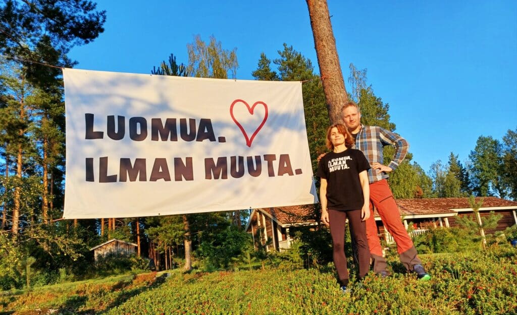 Mies ja nainen ulkona ison banderollin vieressä, banderollissa teksti "Luomua ilman muuta".