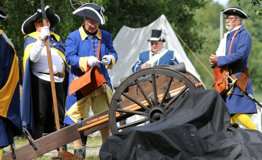 Ryhmä 1700-luvun sotilasasuihin pukeutuneita miehiä seisoo tykin ympärillä.