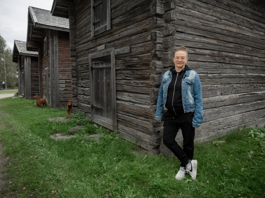 Farkkutakkinen nainen nojaa aitan seinään