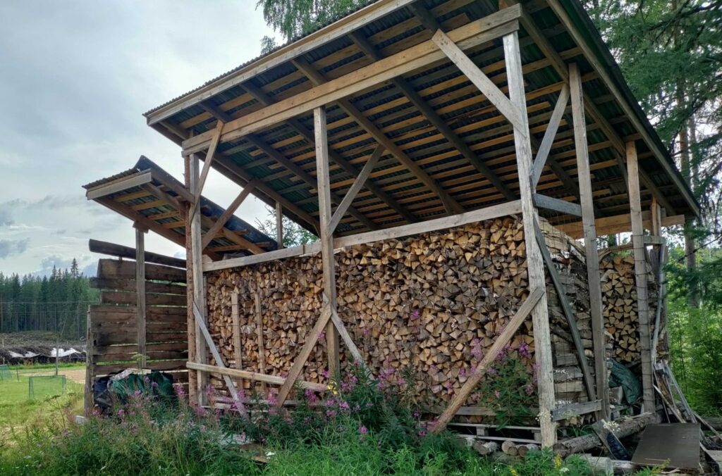 Kesäpäivä, puinen katos, jossa polttopuita.