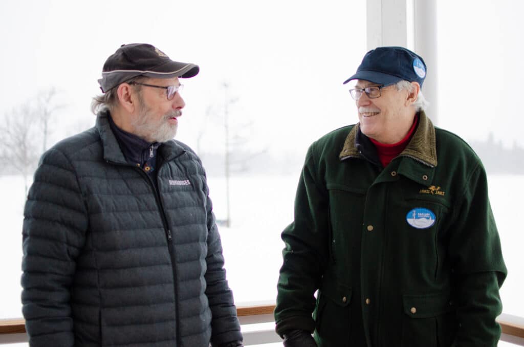 Kaksi miestä seisoo ulkona ja katsoo toisiaan hymyillen.