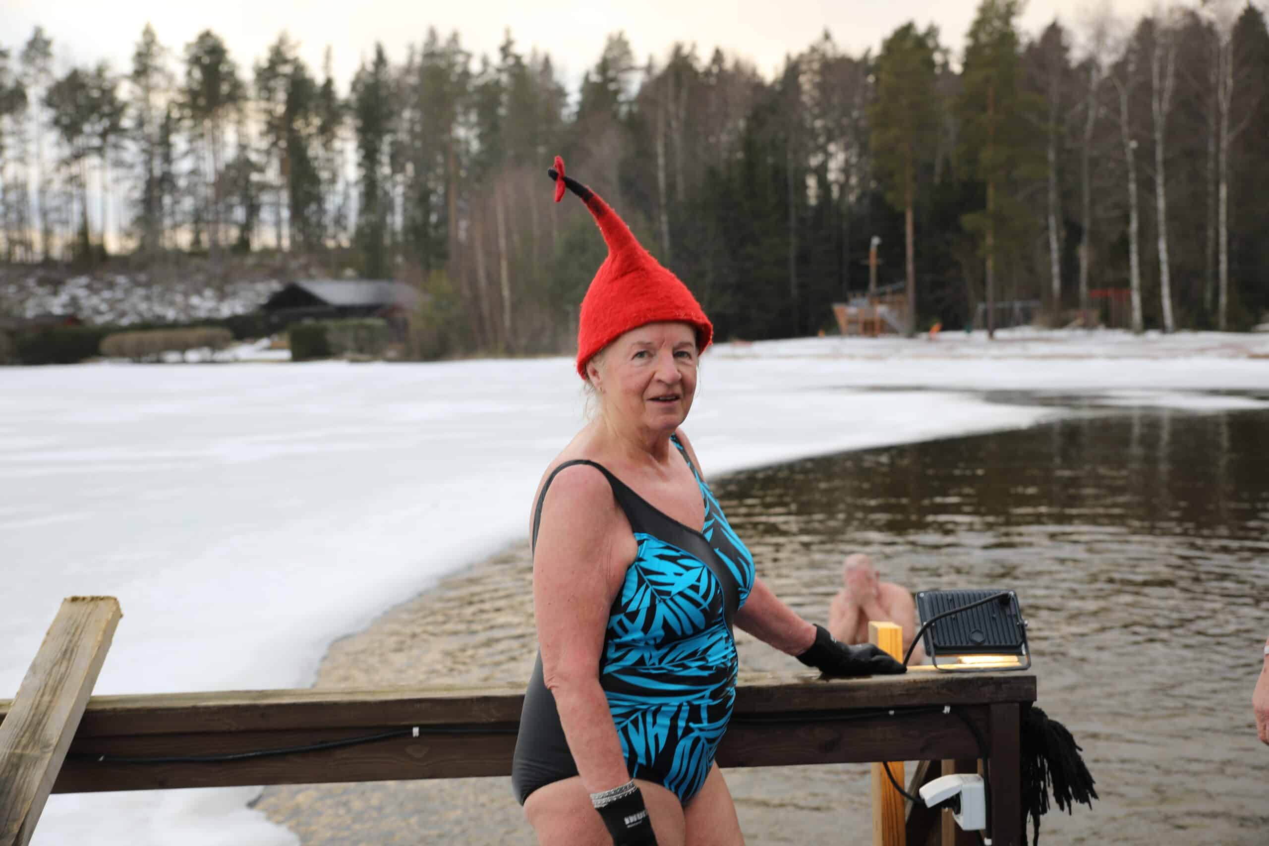 Nainen laiturilla sininen uimapuku päällään ja punainen hattu päässään.