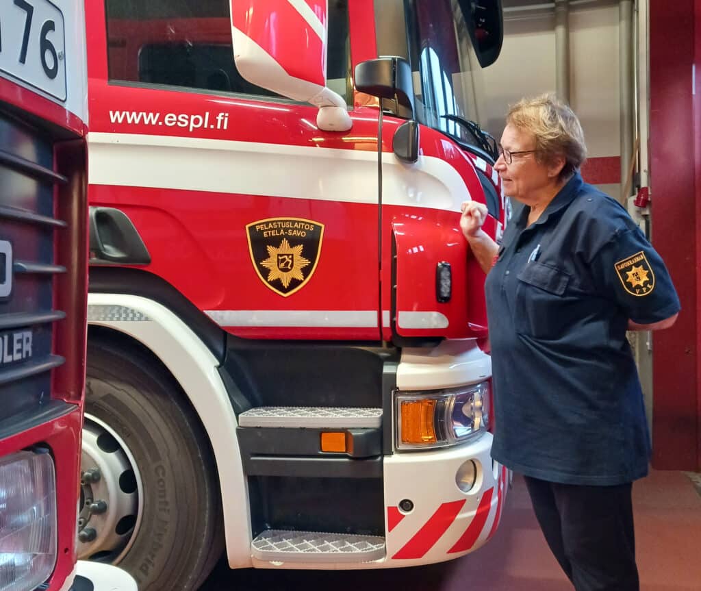 Vapaapalokuntalainen seisoo sinisessä asussa paloauton edessä.