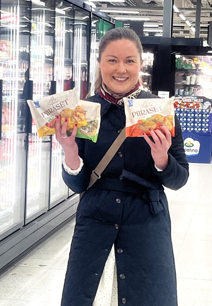 Silpa Kinnunen seisoo Prismassa pakastekaappien edessä käsissään hänen kolmea eri makua olevat piiraspakkaukset.