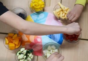 Hedelmäkulhoja, joista kädet kurottelevat hedelmiä.