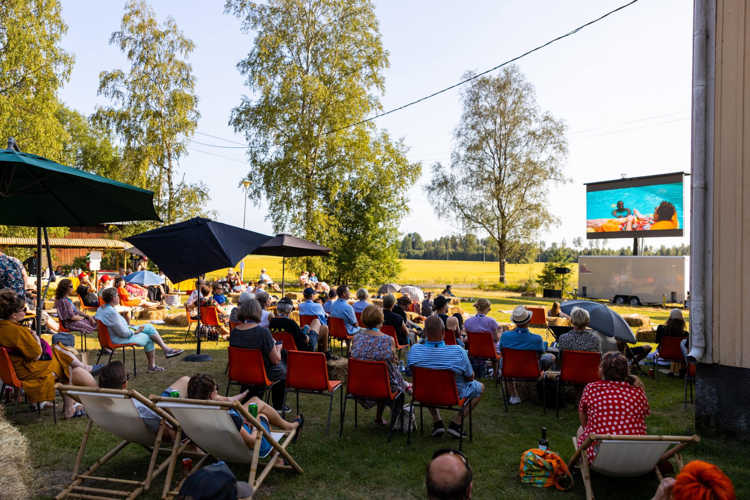 Ihmisiä retkituoleissa katsomassa elokuvaa pellon reunalla.
