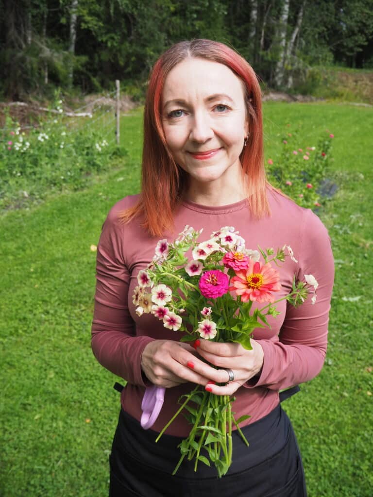 Leikkokukkayrittäjä Eini Laukkanen pitää kukkakimppua käsissään niityn laidalla