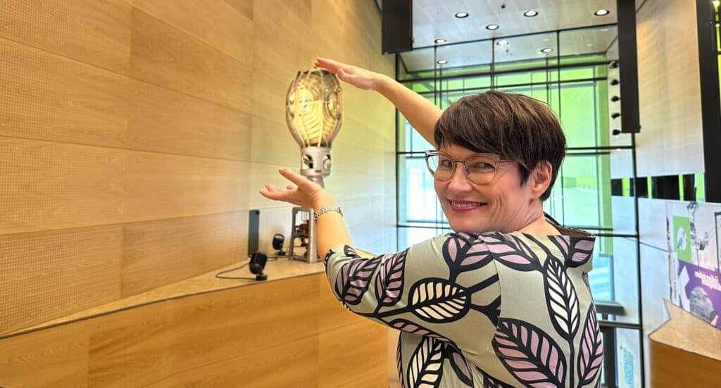 Hymyilevä nainen Merikeskus Vellamon aulassa. Näyttää siltä kuin hän pitelisi majakan lamppua käsissään.