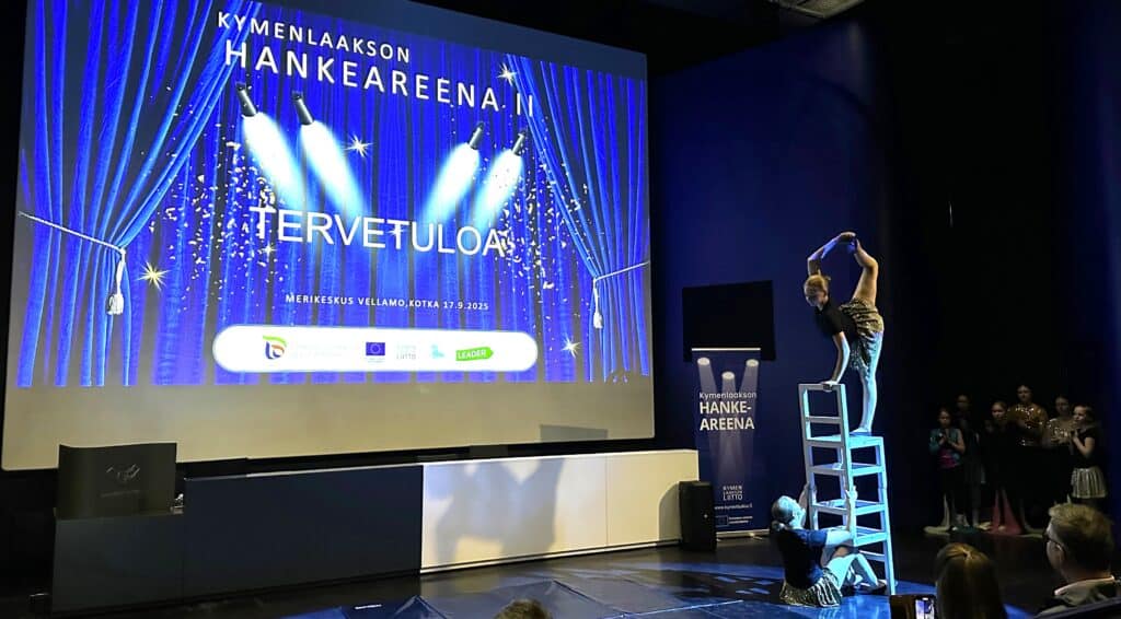 Kuvassa sirkustaiteilijoita temppuilemassa tuolien päällä ja valkokangas, jossa lukee muun muassa Hankeareena.