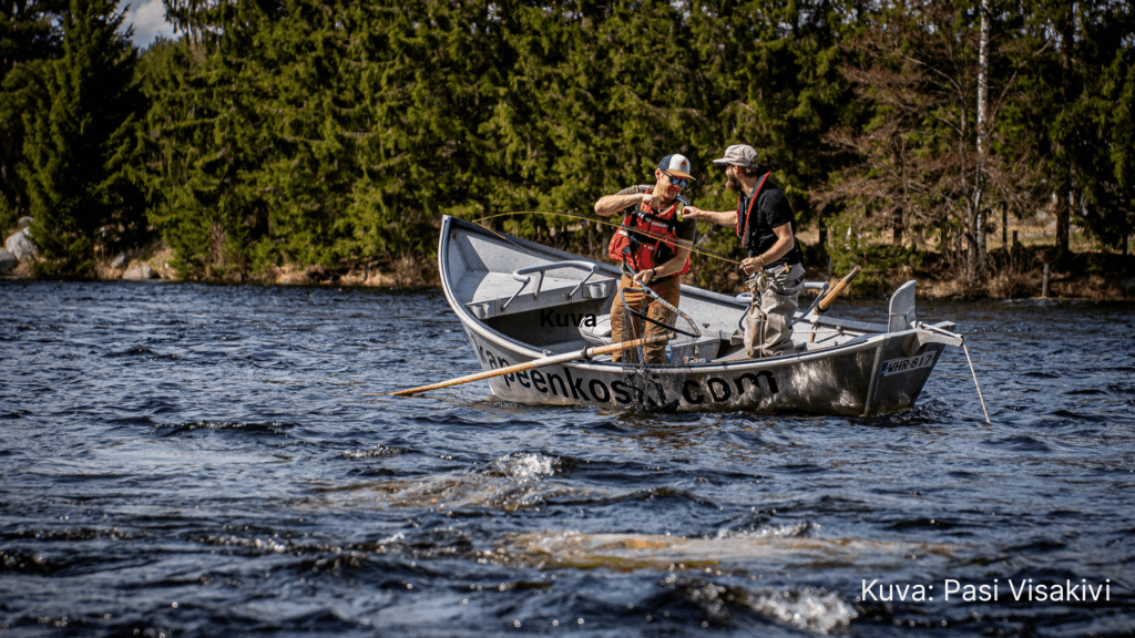 Kaksi miestä kalastusvapojen kanssa veneessä koskessa.