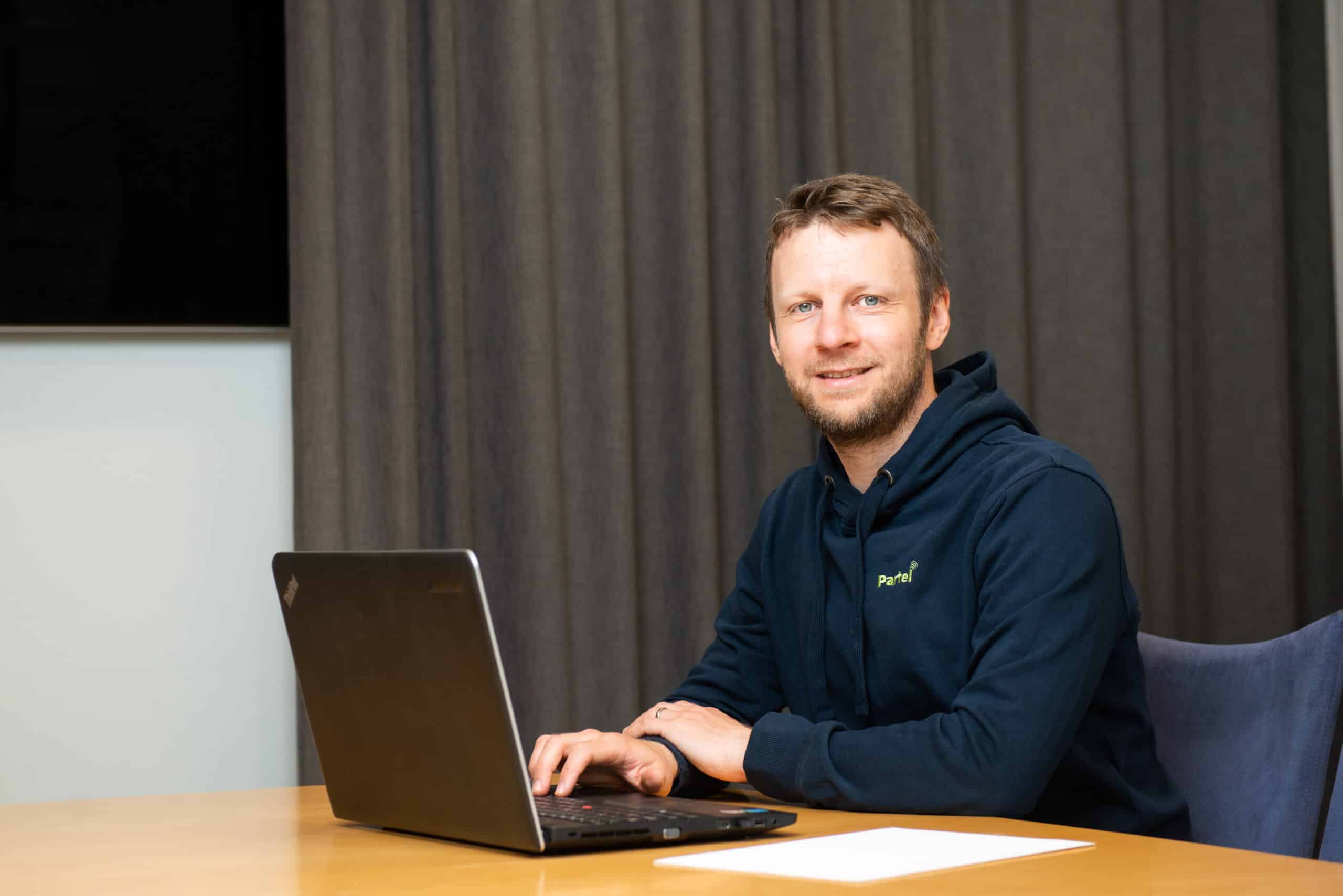 Partelin kehitysjohtaja Fredrik Albrecht istuu kannettavan tietokoneen ääressä ja hymyilee kameralle.