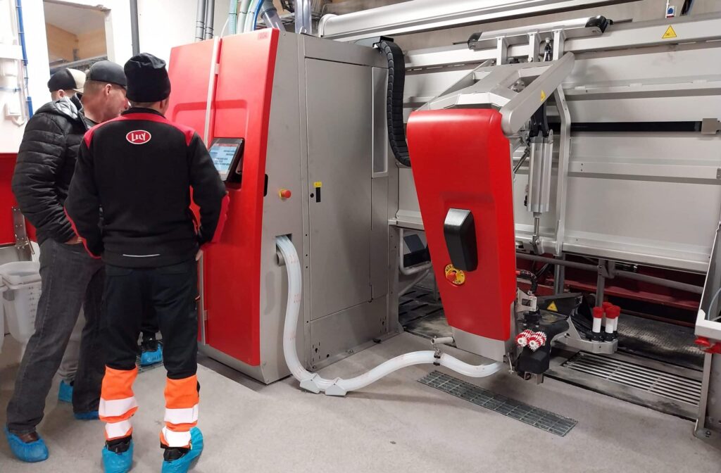 kolme ihmistä tarkastelee lypsyrobotin konehuonetta