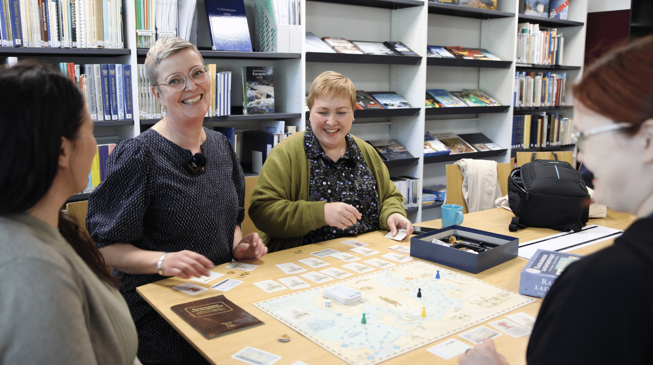 Iloiset ihmiset pelaavat lautapeliä kirjastossa.