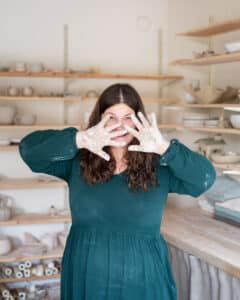 Mekkon pukeutunut pitkähiuksinen nainen näyttää kämmeniään keramiikkapajassa.