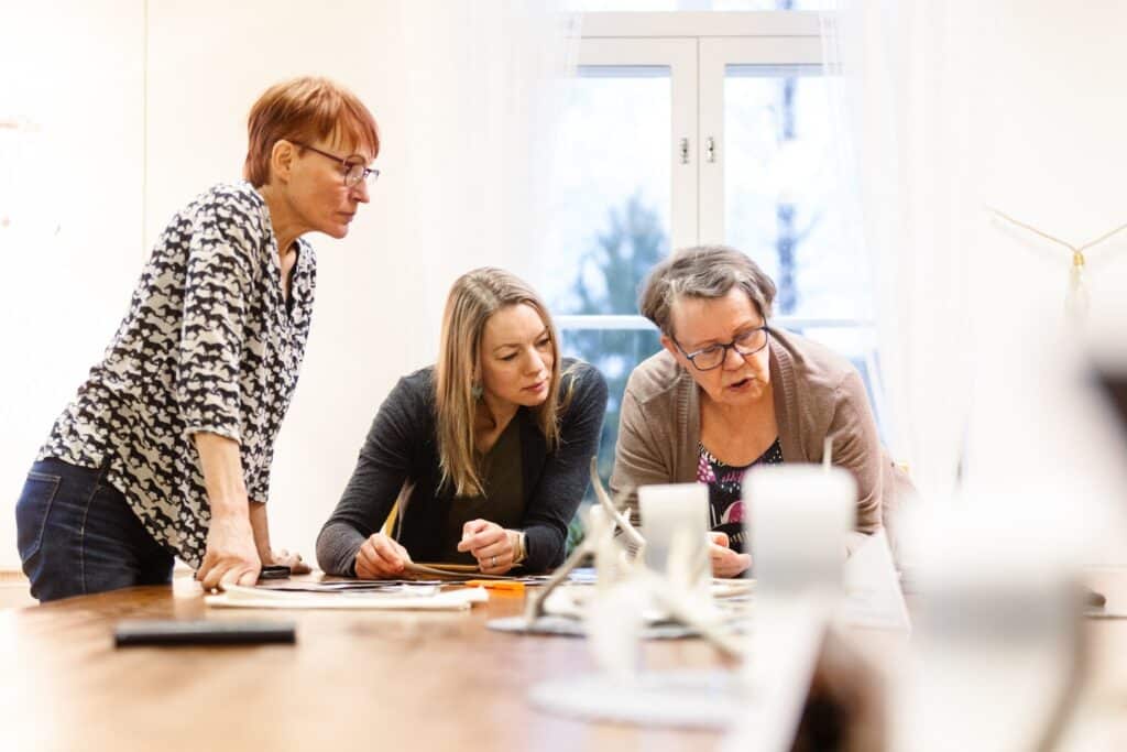 Kolme niaista valoisassa huoneessa katselevat valokuvia pyödän ääressä.