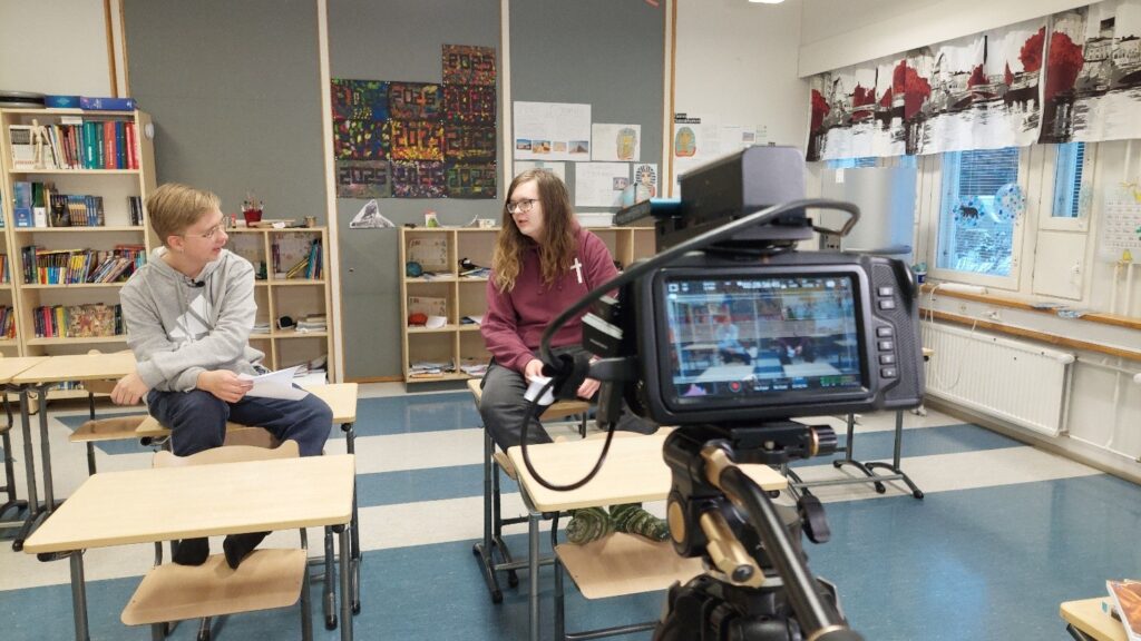 Kaksi nuorta miestä istumassa pulpeteilla kameran edessä ja kertomassa itselleen tärkeistä asioista.