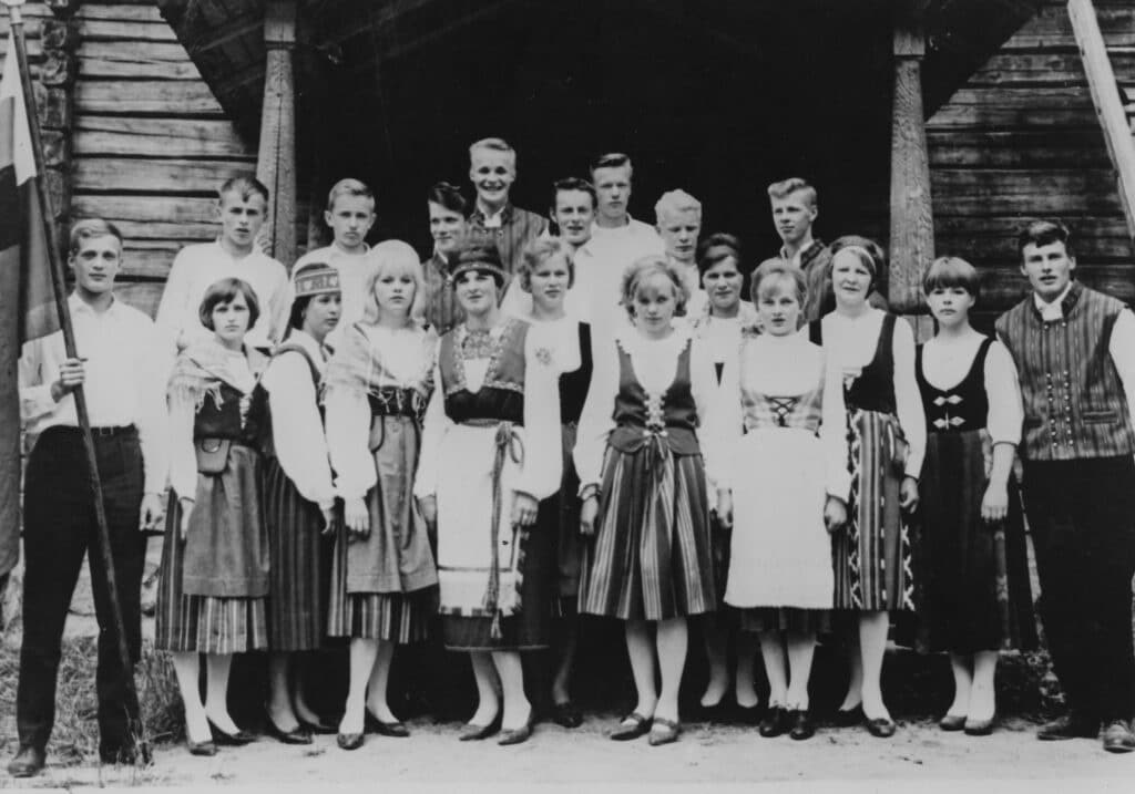 Mustavalkoinen kuva, iso joukko kansallispukuihin pukeutuneita nuoria ihmisiä poseeraa kameralle.