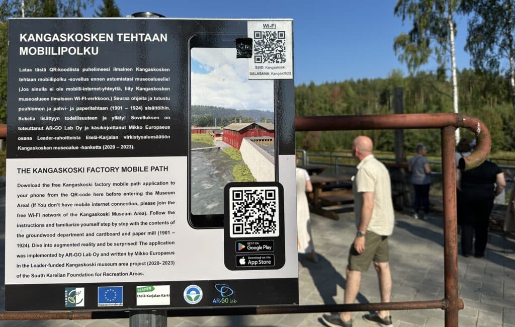 Mobiilipolun opaskyltti, taustalla ihmisiä