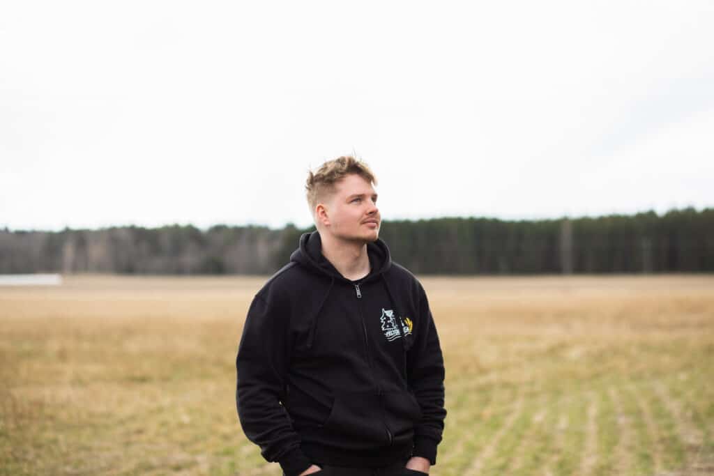 Mies seisoo pellon edessä, katse kameran ohi