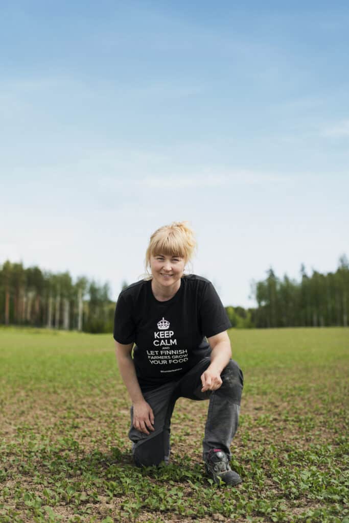Anna Johansson seisoo toisen polven varassa pellon edustalla ja hymyilee