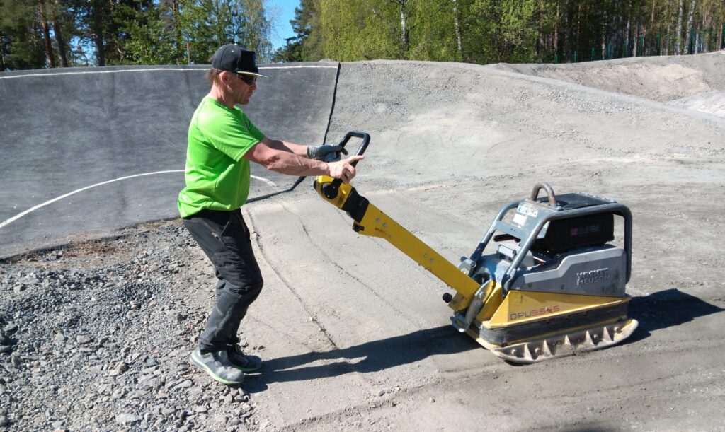 Mies tasoittaa BMX-radan maapohjaa työnnettävällä tasoituskoneella.