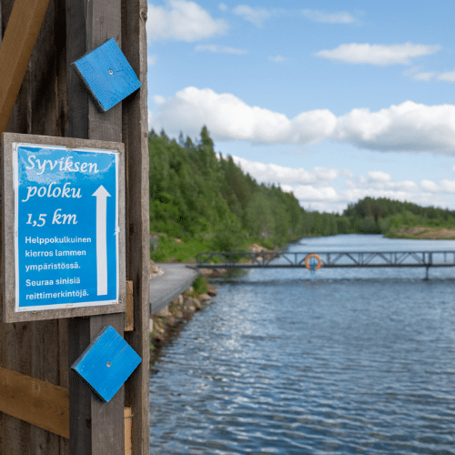 Vesialue, jota halkoo silta. Kyltti, jossa lukee "Syviksen polku 1,5km".