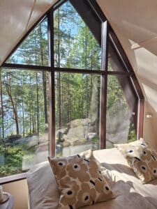 Mökin ikkunasta avautuu metsämaisema, ikkunan edessä vuode.