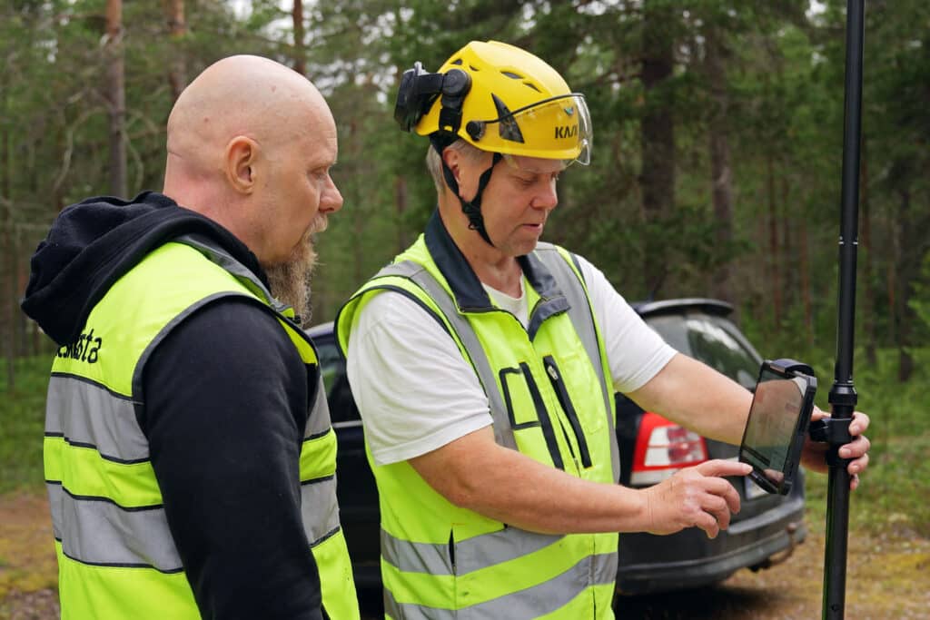 Valokuituverkon rakentajat käyttävät mittauslaitetta työmaalla metsän keskellä. Fibernätsbyggare använder mätutrustning på en arbetsplats i skogen.